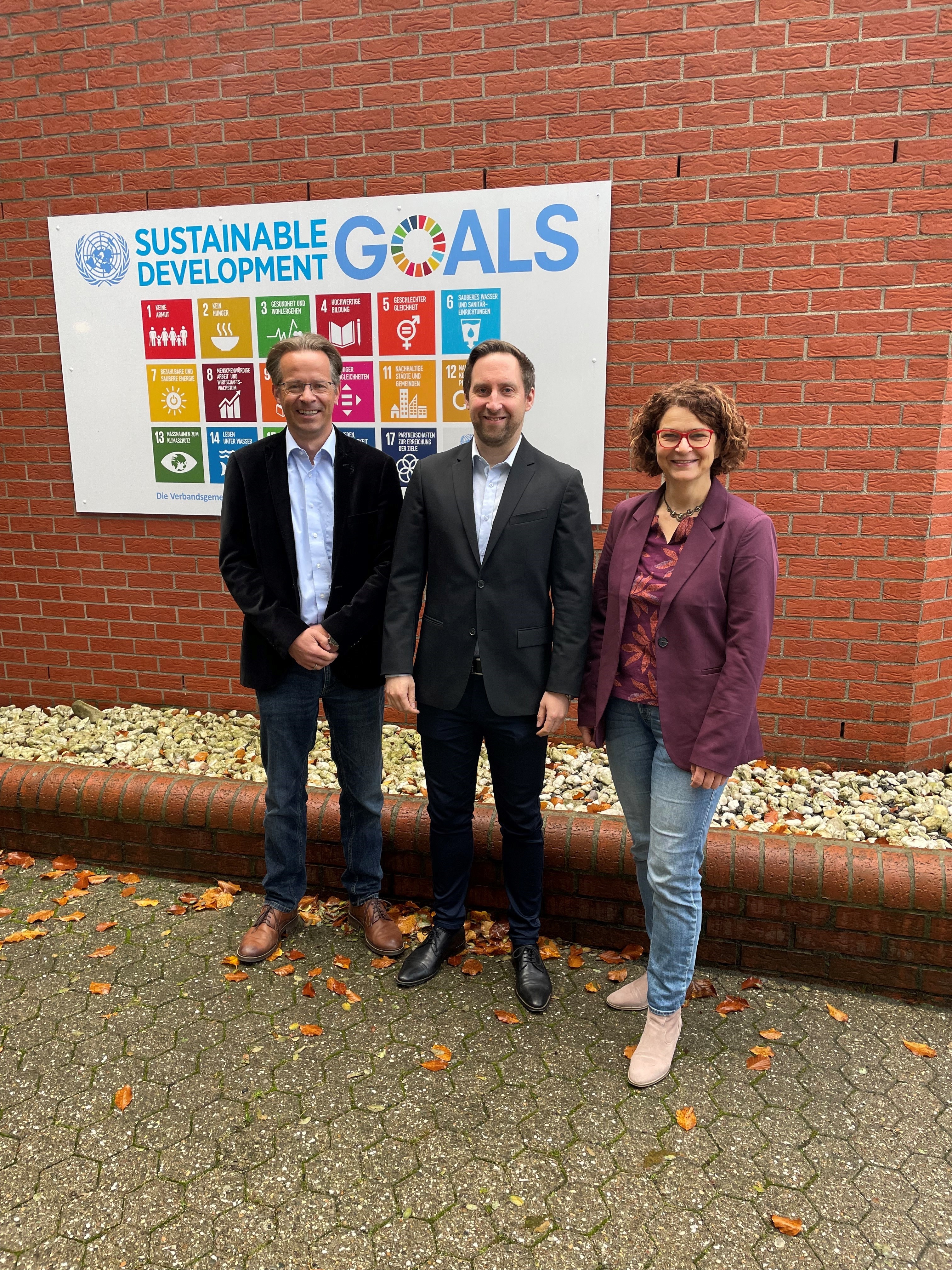 Der Erste Beigeordnete Marco Dörner, Nachhaltigkeitskoordinator Timo Karl und die Bürgermeisterin der Verbandsgemeinde Hachenburg, Gabriele Greis (v.l.n.r.), vor den Nachhaltigkeitszielen der Vereinten Nationen, die einen wichtigen Handlungsleitfaden für die Verwaltung der Verbandsgemeinde darstellen. 