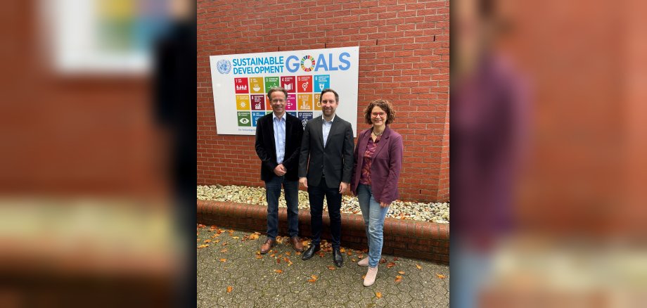 Der Erste Beigeordnete Marco Dörner, Nachhaltigkeitskoordinator Timo Karl und die Bürgermeisterin der Verbandsgemeinde Hachenburg, Gabriele Greis (v.l.n.r.), vor den Nachhaltigkeitszielen der Vereinten Nationen, die einen wichtigen Handlungsleitfaden für die Verwaltung der Verbandsgemeinde darstellen. 