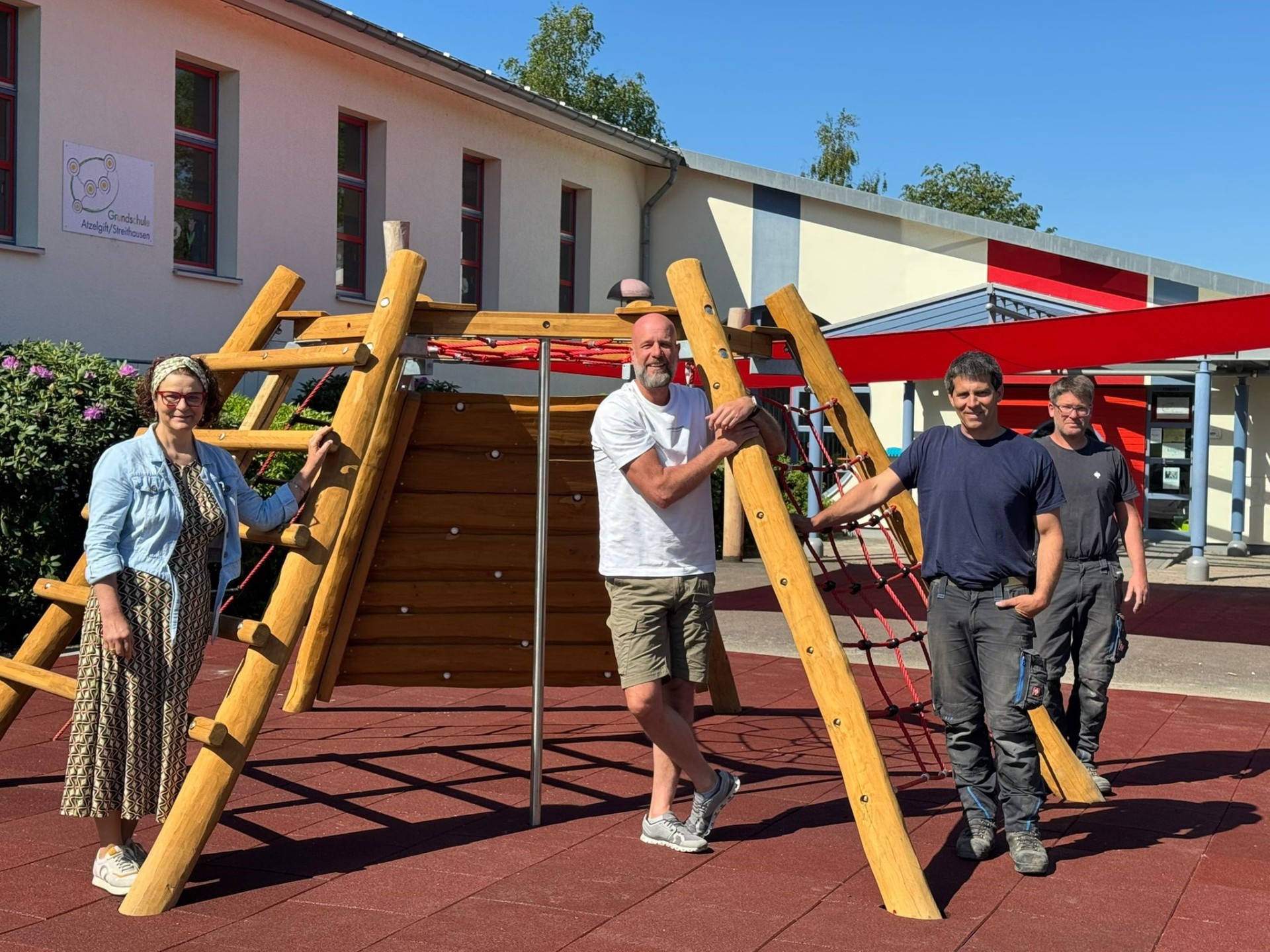 Gruppenfoto von Bürgermeisterin Gabriele Greis, Schulleiter Daniel Busch und Mitarbeiter des Bauhofes (v. l. n. r.) vor dem Sonnensegel der Grundschule Atzelgift-Streithausen