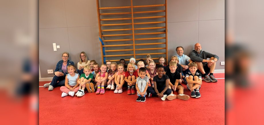 Kinder sitzen auf dem Boden in der Sporthalle der Grundschule Atzelgift-Streithausen