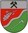Unter silbernem Schildhaupt, darin schräggekreuzt ein schwarzer Schlägel und ein schwarzer Hammer, schräglinks geteilt durch eine silberne Wellenleiste von Rot und Grün. Ob ein gestürztes silbernes Eichenblatt mit Eicheln. Unten schräg aufgerichtet eine silberne Rodungshacke.